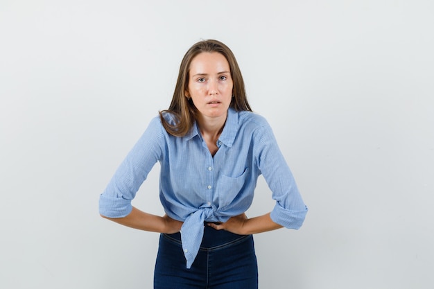 Jonge dame die lijdt aan buikpijn in blauw shirt, broek en op zoek wegkwijnen.