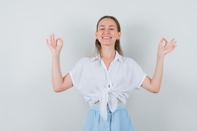 Jonge dame die meditatiegebaar in blouse en rok toont en blij kijkt