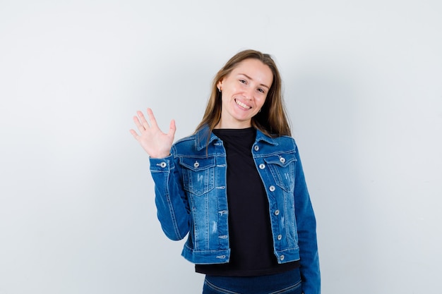 Jonge dame die met de hand zwaait voor begroeting in blouse en er blij uitziet. vooraanzicht.