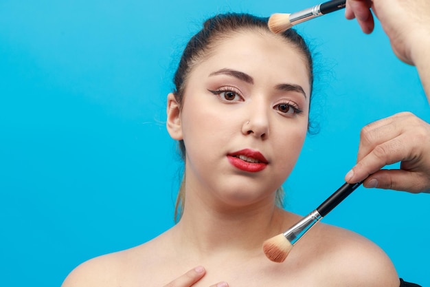 Jonge dame die naar de camera kijkt en make-upartiest die make-up voor haar doet