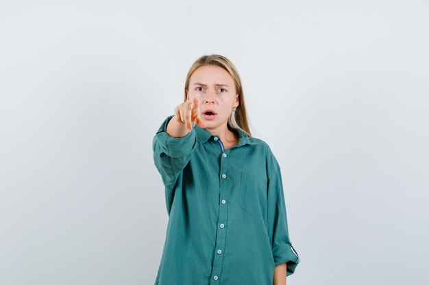 Jonge dame die naar de camera wijst in een groen shirt en er serieus uitziet