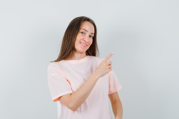 Jonge dame die naar de rechterbovenhoek in roze t-shirt wijst en joviaal kijkt