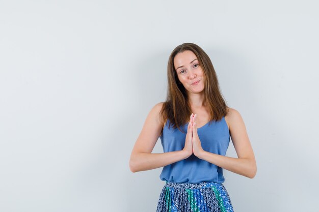 Jonge dame die namaste-gebaar in hemd, rok toont en er schattig uitziet