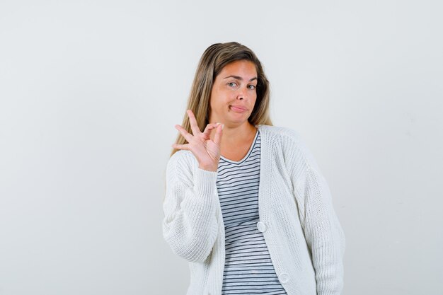 Jonge dame die ok gebaar in t-shirt, jasje toont en zelfverzekerd, vooraanzicht kijkt.