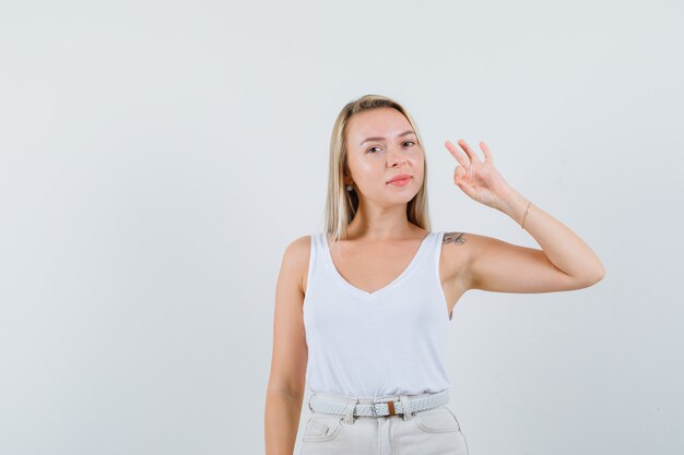 Jonge dame die ok gebaar in witte blouse toont en verrukkelijk kijkt