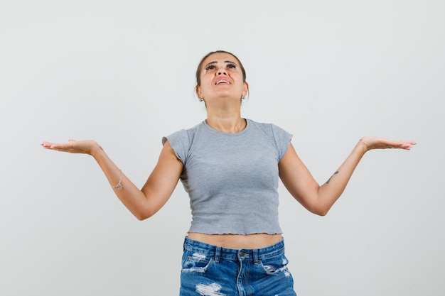 Gratis foto jonge dame die omhoog kijkt, armen in t-shirt, korte broek spreidt en hoopvol kijkt