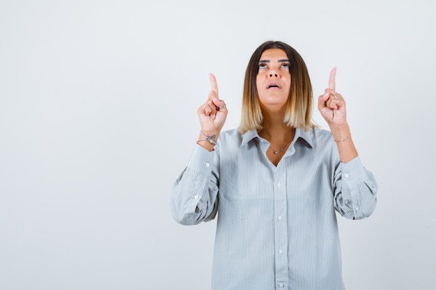 Jonge dame die omhoog wijst in een oversized shirt en er zelfverzekerd uitziet, vooraanzicht.