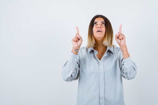 Jonge dame die omhoog wijst in een oversized shirt en er zelfverzekerd uitziet, vooraanzicht.