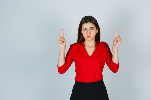 Jonge dame die omhoog wijst terwijl het blazen van wangen in rode blouse, rok en weemoedig kijkt