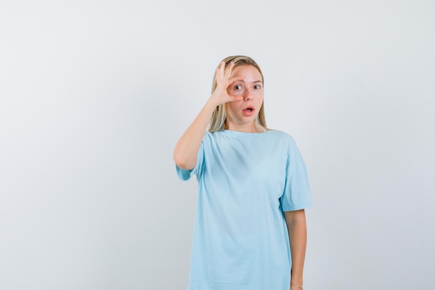 Jonge dame die oog opent om duidelijk in t-shirt te zien en er verward geïsoleerd uitziet