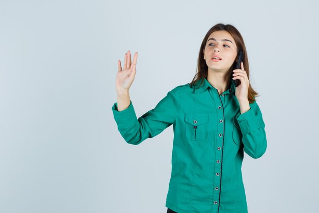 Jonge dame die op mobiele telefoon spreekt, stopgebaar in groen overhemd toont en er zelfverzekerd uitziet. vooraanzicht.