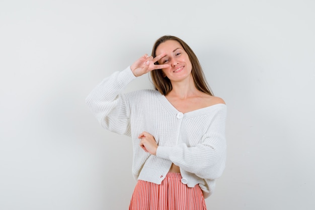 Jonge dame die overwinningsteken in vest en rok toont die zalig geïsoleerd kijken