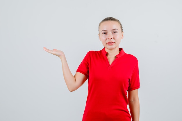 Jonge dame die palm opheft als iets vangen in een rood t-shirt en er vrolijk uitzien