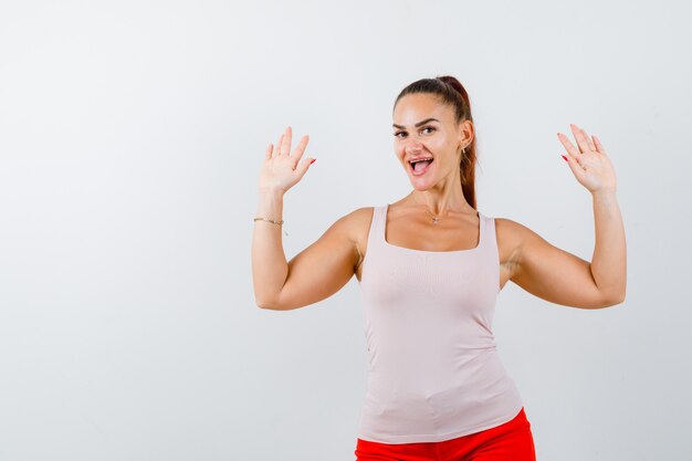 Jonge dame die palmen in overgavegebaar in beige tanktop toont en gelukkig kijkt