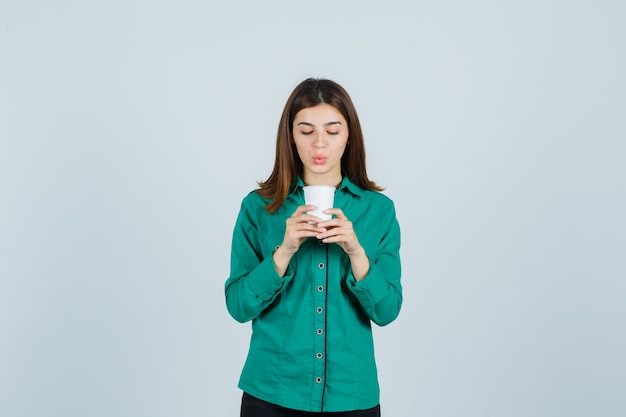 Jonge dame die plastic kop van koffie in overhemd houdt en gericht, vooraanzicht kijkt.