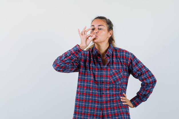 Jonge dame die smakelijk gebaar in geruit overhemd toont en verrukt, vooraanzicht kijkt.