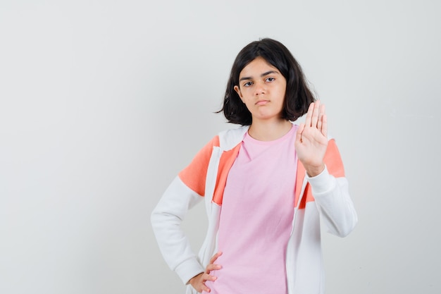 Jonge dame die vaarwel gebaar in jasje, roze overhemd toont en ernstig kijkt.