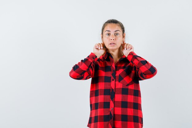 Jonge dame die vingers achter de oren in casual overhemd houdt en nieuwsgierig kijkt. vooraanzicht.