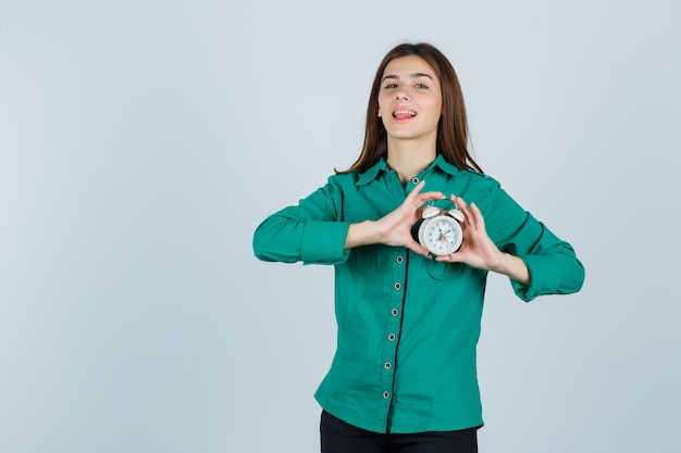 Jonge dame die wekker in overhemd houdt en mooi kijkt. vooraanzicht.