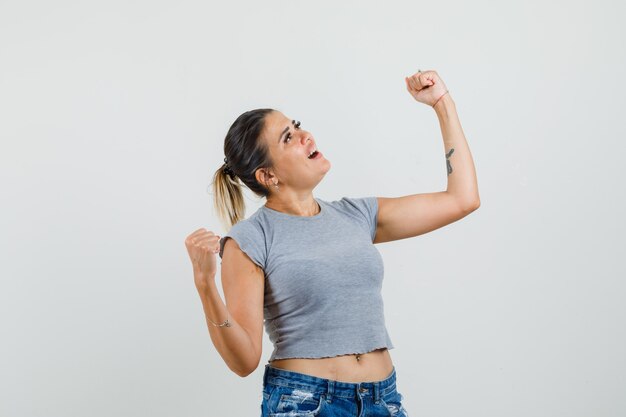 Jonge dame die winnaargebaar in t-shirt, korte broek toont en zalig kijkt.