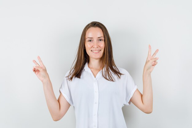 Jonge dame die winnaargebaar in witte blouse toont en blij kijkt.