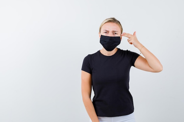 Jonge dame die zelfmoordgebaar maakt in t-shirt, broek, medisch masker en er hopeloos uitziet