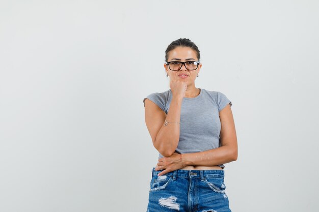 Jonge dame die zich in het denken bevindt stelt in t-shirt, korte broek en ziet er intelligent uit.