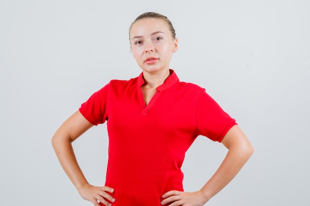 Jonge dame die zich met handen op taille in rood t-shirt bevindt en zelfverzekerd kijkt