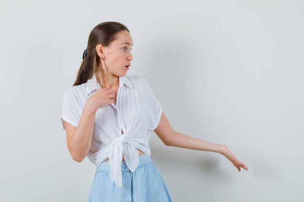 Jonge dame die zich uitstrekt hand in vragend gebaar in blouse en rok en op zoek gericht