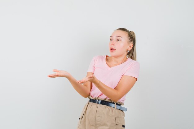 Jonge dame die zich uitstrekt handen in verbaasd gebaar in t-shirt en broek vooraanzicht