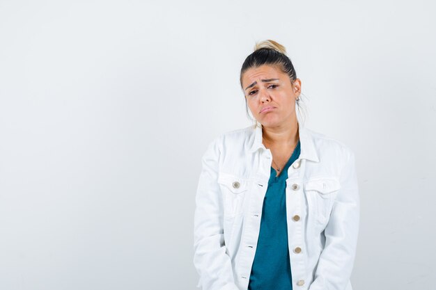 Jonge dame die zich voordeed in shirt, witte jas en teleurgesteld kijkt, vooraanzicht.