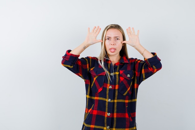 Gratis foto jonge dame doet grappig gebaar in geruit overhemd en ziet er schattig uit, vooraanzicht.