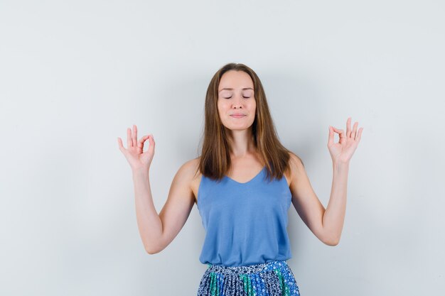 Jonge dame doet meditatie met gesloten ogen in hemd, rok en ziet er vredig uit