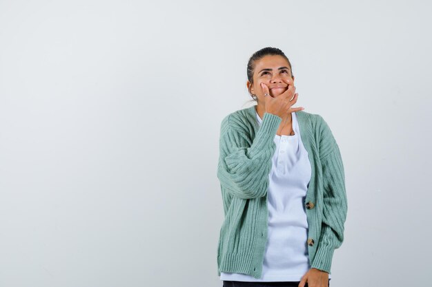 Jonge dame drukt op wangen met vingers in t-shirt, jasje en ziet er schattig uit