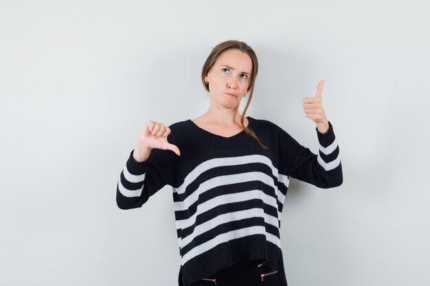 Jonge dame duimen op en neer in casual shirt tonen en aarzelend op zoek