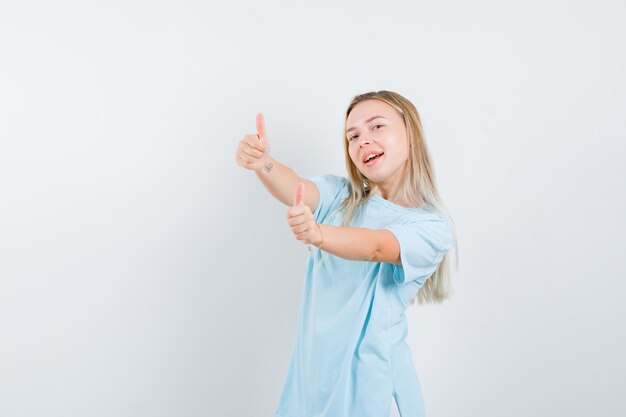 Jonge dame duimen opdagen in t-shirt en op zoek gelukkig, vooraanzicht.