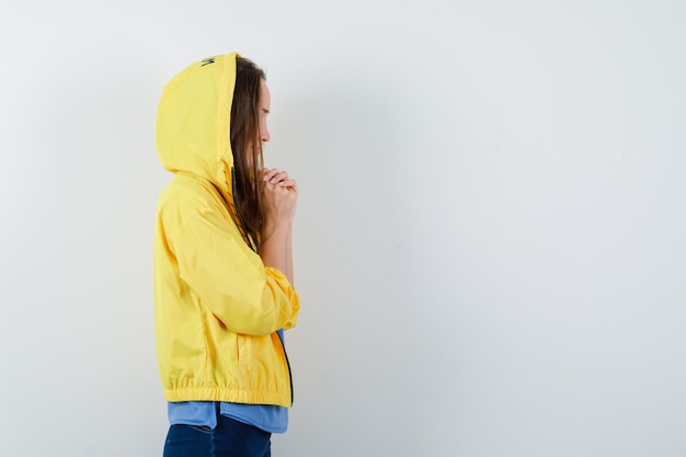 Jonge dame hand in hand gevouwen tijdens het bidden in t-shirt, jas en hoopvol kijken.