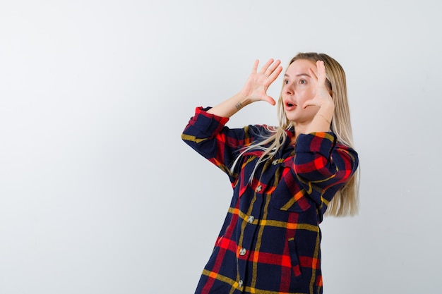 Jonge dame hand in hand in de buurt van gezicht om duidelijk te zien in geruit overhemd en op zoek verbaasd, vooraanzicht.