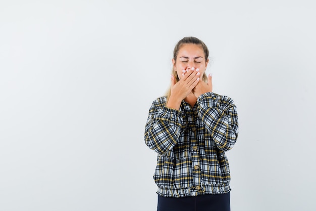 Jonge dame hand in hand op de mond in shirt, korte broek en peinzend op zoek. vooraanzicht.