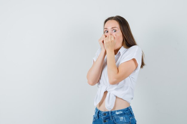 Jonge dame hand in hand op haar mond in witte blouse en kijkt opgewonden, vooraanzicht.