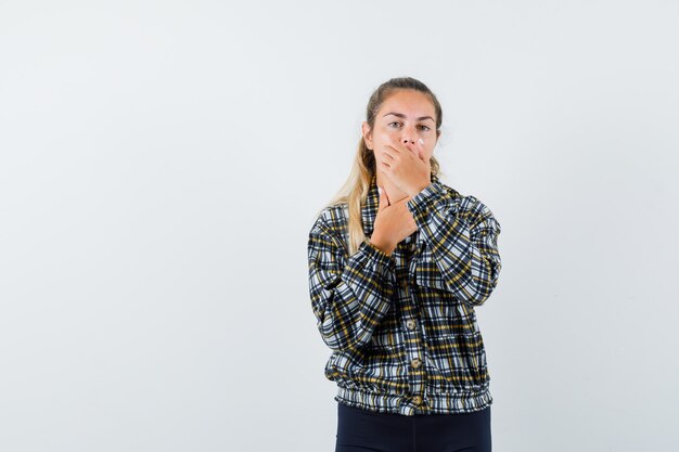 Jonge dame hand op mond in shirt, korte broek en op zoek verbaasd, vooraanzicht.