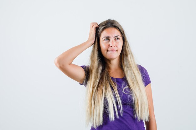 Jonge dame hoofd krabben in violet t-shirt en besluiteloos, vooraanzicht op zoek.