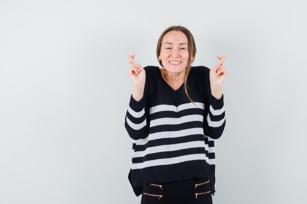 Jonge dame houdt vingers gekruist in casual shirt en ziet er vrolijk uit