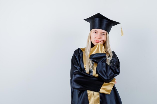 Jonge dame in academische jurk die in denkende pose staat en er attent uitziet