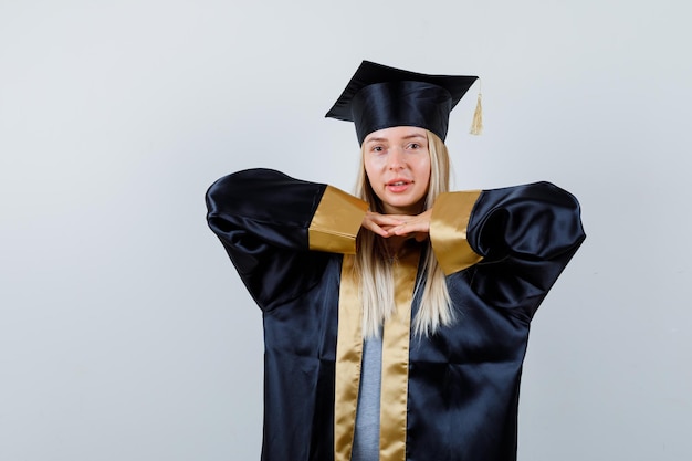 Jonge dame in academische jurk hand in hand onder de kin en ziet er prachtig uit