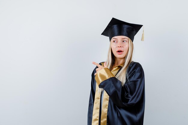 Jonge dame in academische kleding die naar de linkerkant wijst en verbaasd kijkt