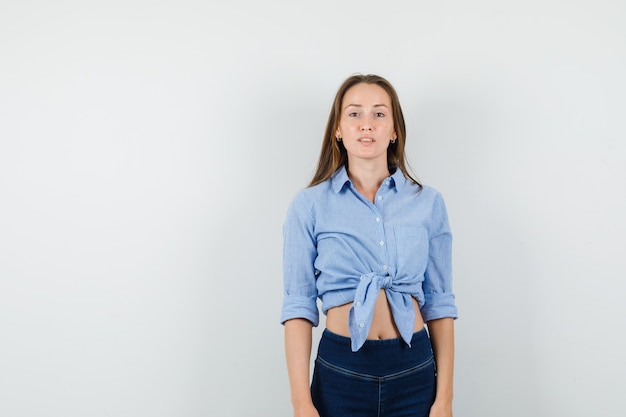 Gratis foto jonge dame in blauw shirt, broek camera kijken en gevoelloos op zoek