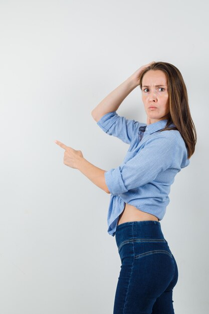 Jonge dame in blauw shirt, broek wijst weg en kijkt verward