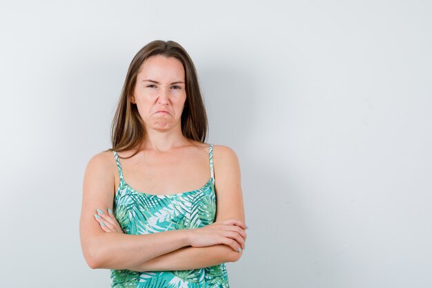 Jonge dame in blouse die met gekruiste armen staat terwijl ze het gezicht fronst en boos kijkt, vooraanzicht.