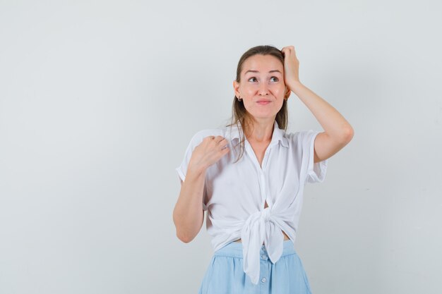 Jonge dame in blouse en rok die hoofd krabt en aarzelend kijkt